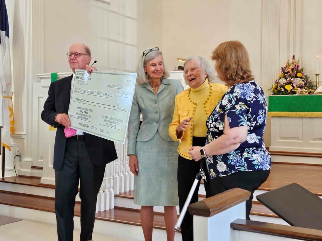 four adults stand at front of church with large paper check for $10,000