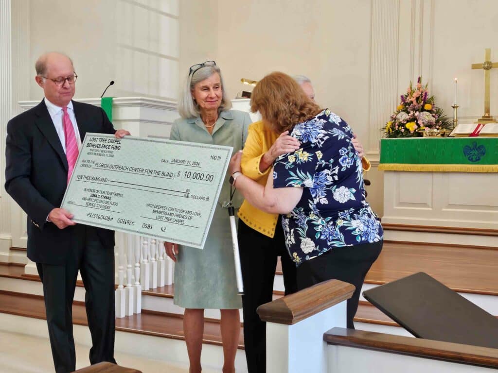 4 people hold up paper check and two of the people are hugging