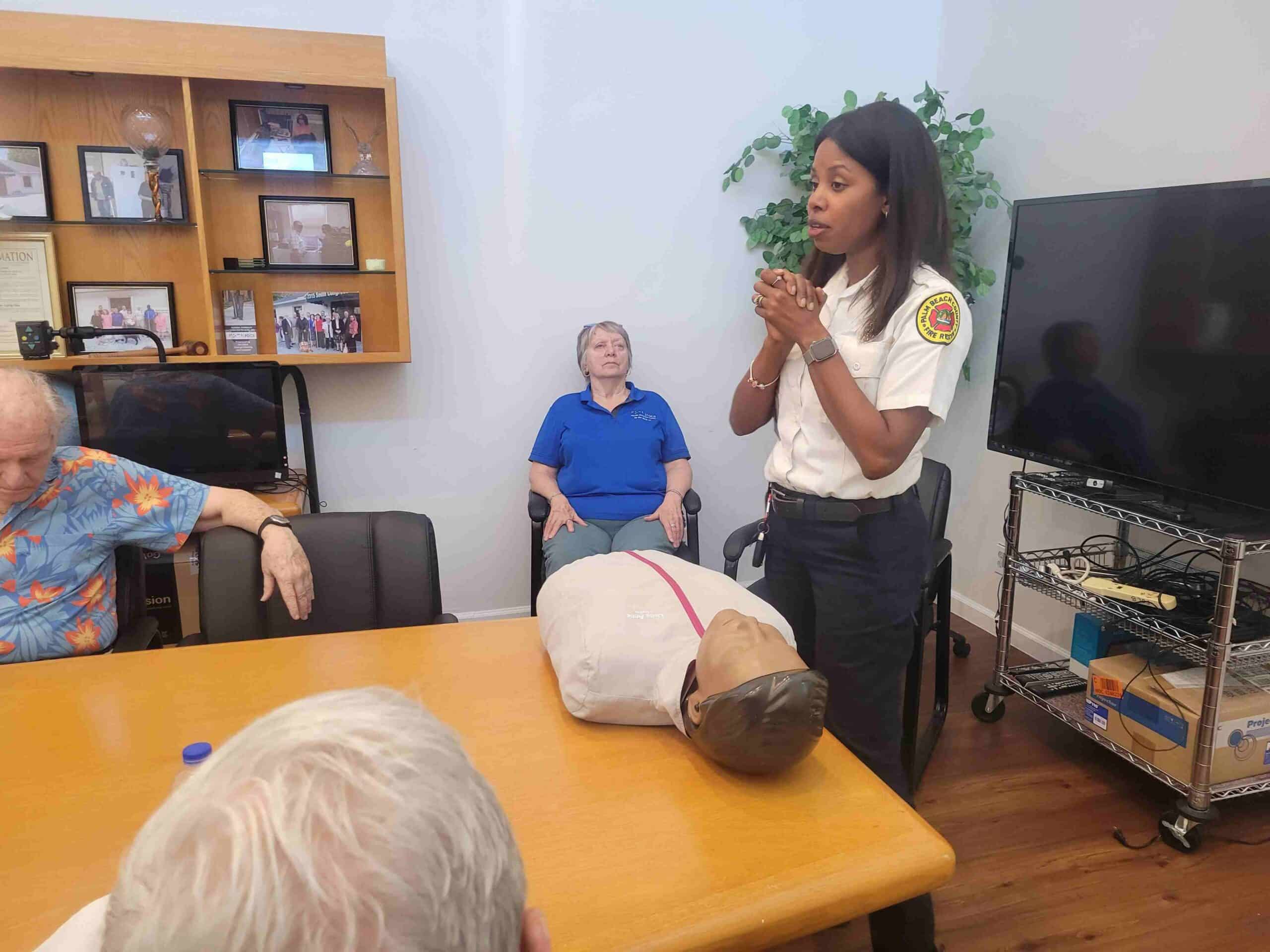 woman CPR instructor speaks to group of adults with CPR dummy in front of her