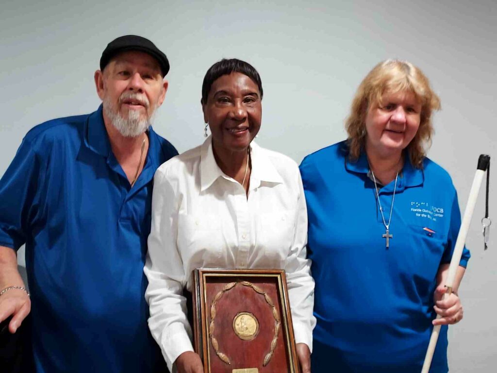 Woman holding certificate stands between man and woman holding a white cane