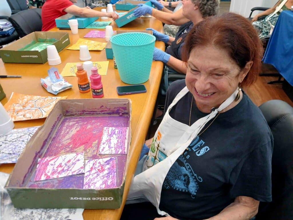 woman in apron smiles while showing off artwork