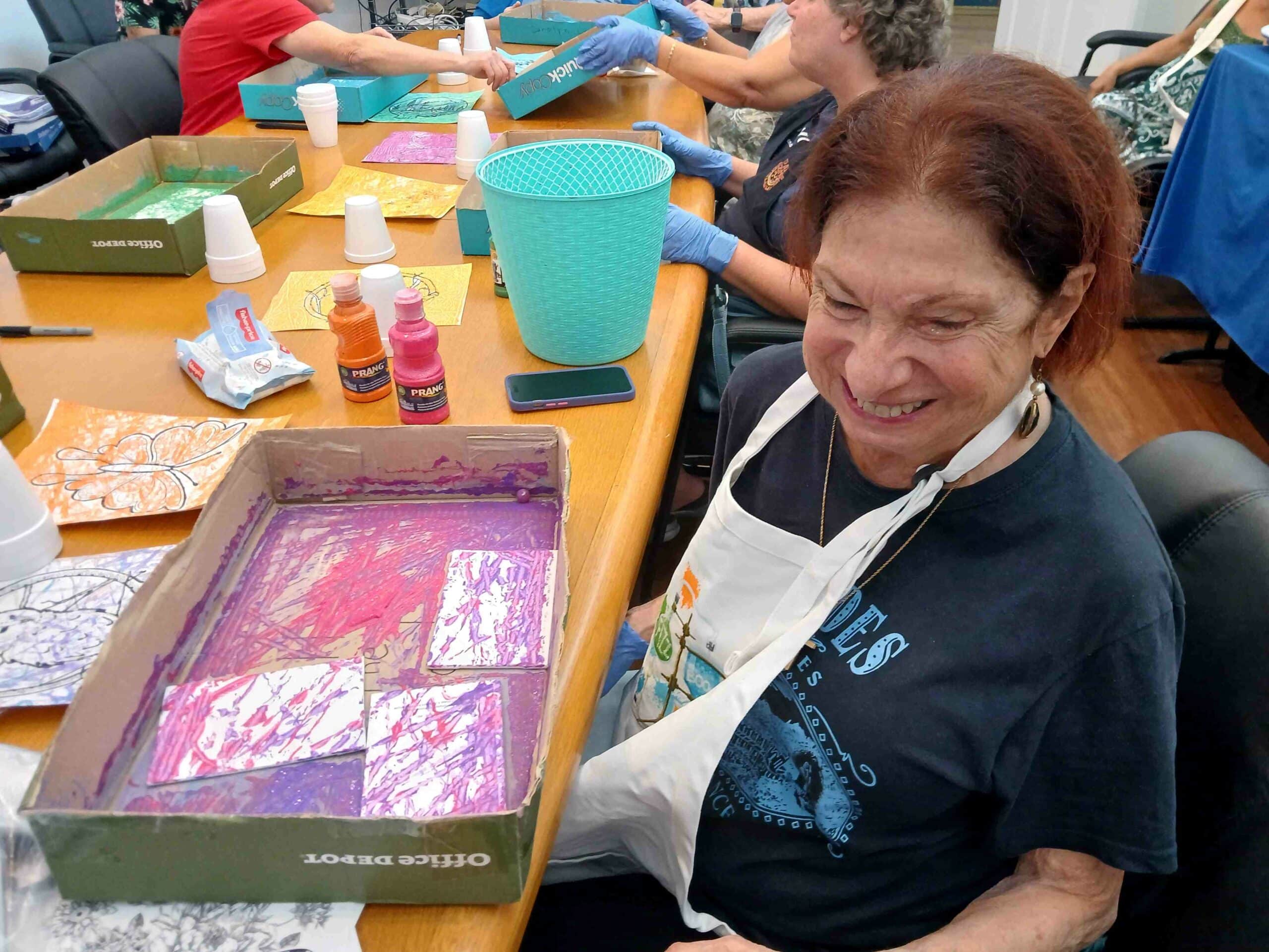 woman in apron smiles while showing off artwork