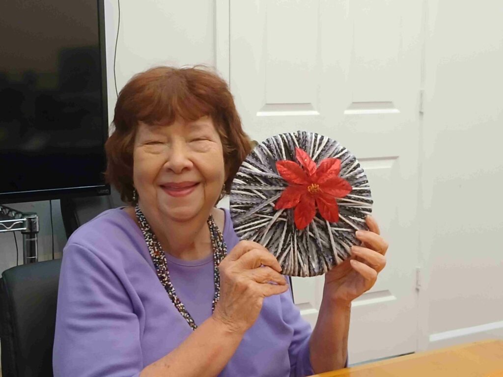Woman in purple shirt holds up yarn and flower craft