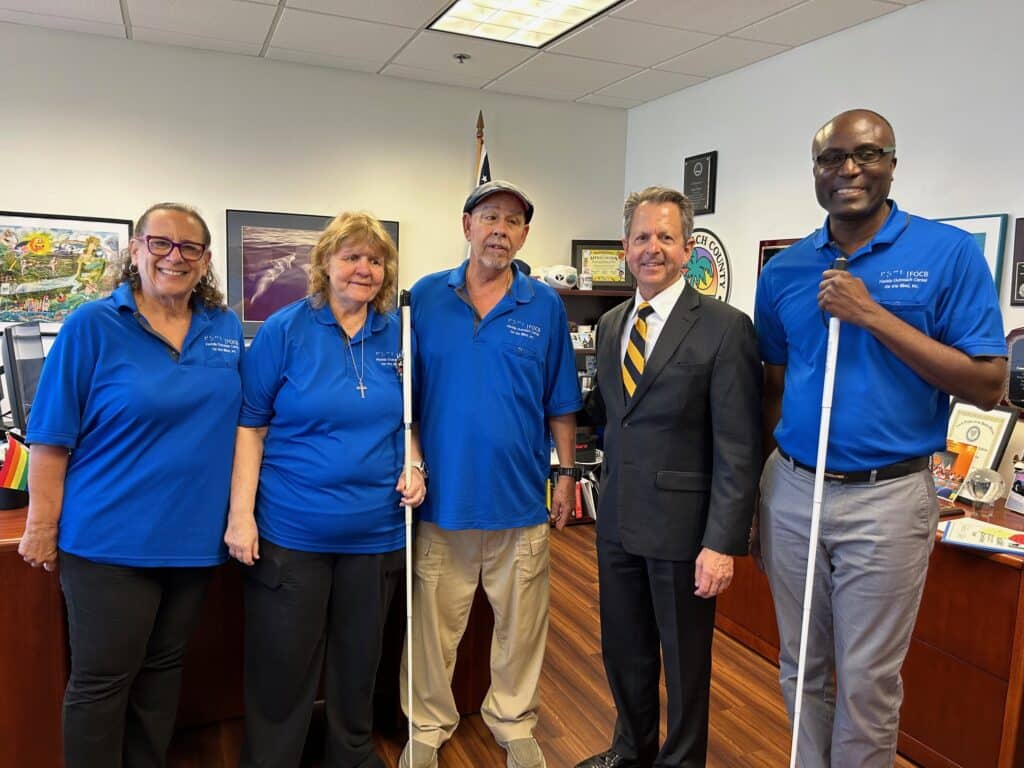 Four adults in blue polo shirts stand with man in black suit and tie.