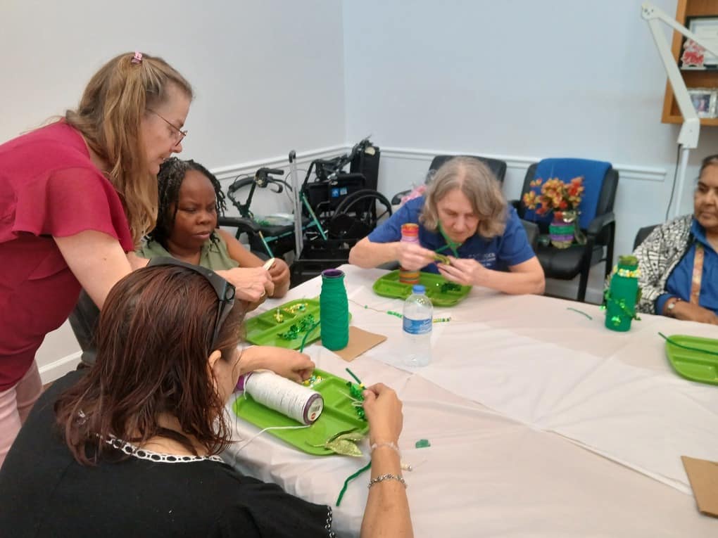 group of adults sit around a conference table crafting while woman stands to help