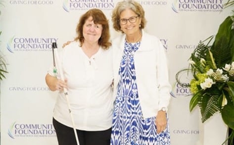 woman with white cane stands next to woman in blue dress