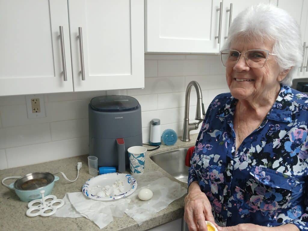 woman smiles with hardboiled egg in hand and air fryer in background