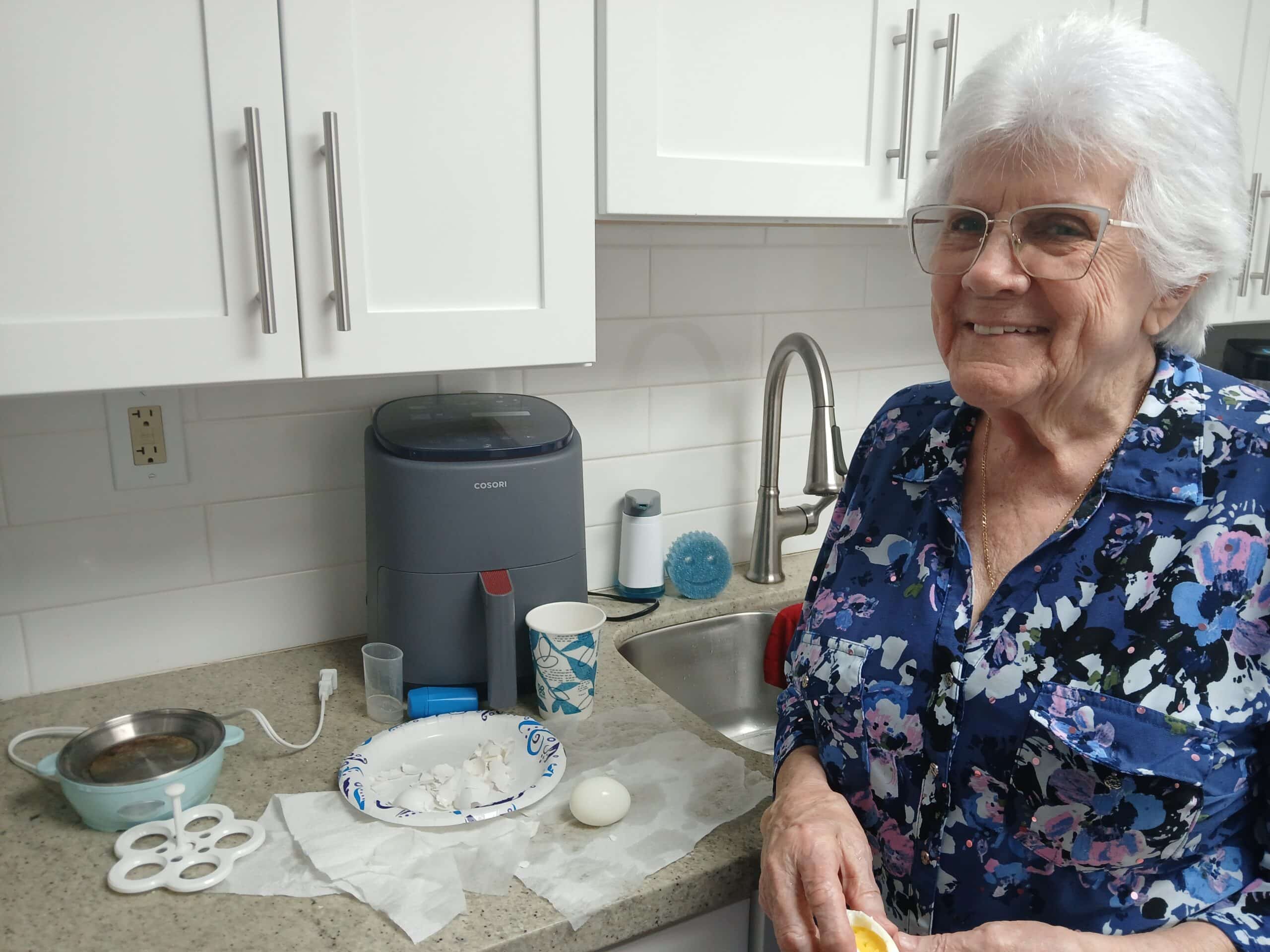 woman smiles with hardboiled egg in hand and air fryer in background