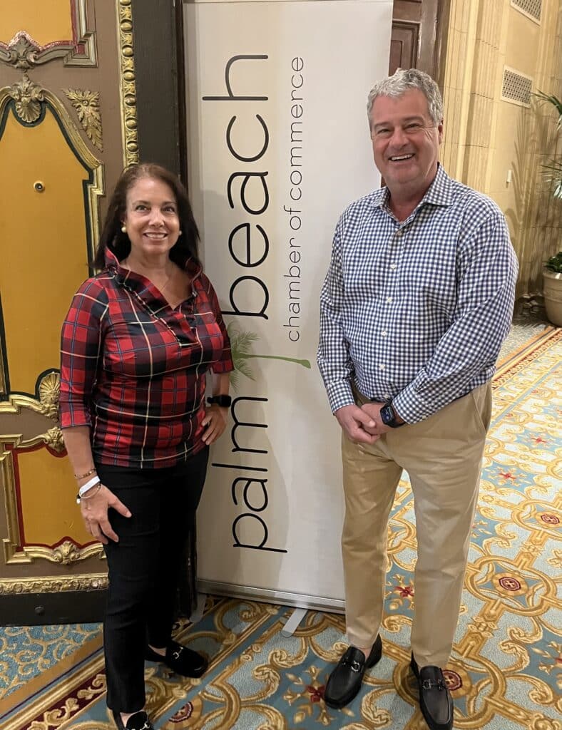 woman and man stand next to palm beach chamber sign