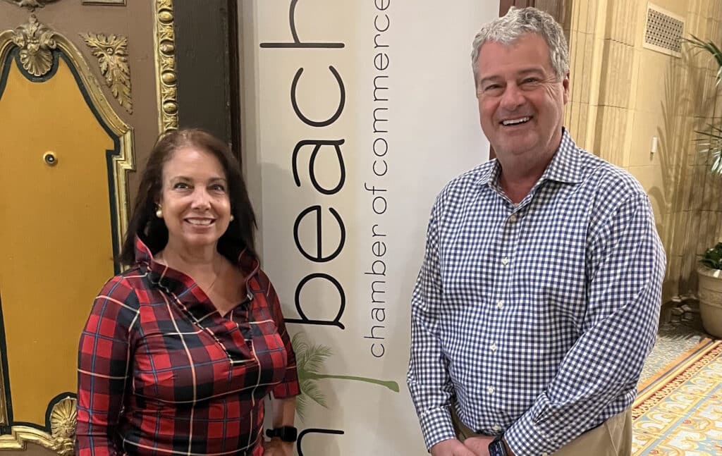 woman and man stand next to palm beach chamber sign