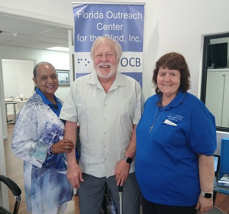 Man stands between two women while smiling and holding a white cane