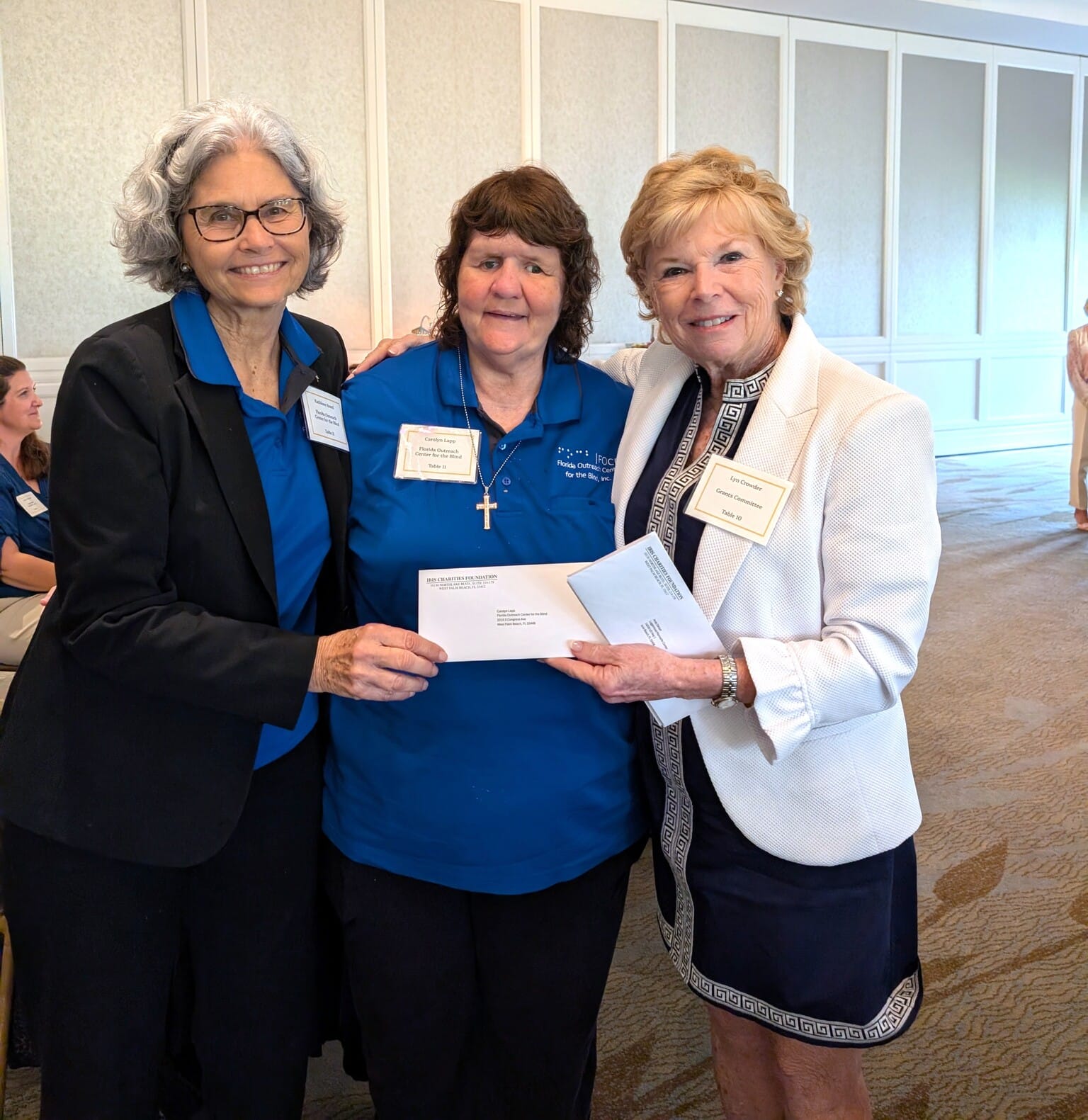 three women pose for picture holding an envelope up on display