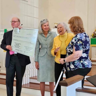 four adults stand at front of church with large paper check for $10,000