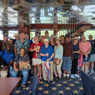 large group of adults some with white canes stand in side a yacht and pose for a picture