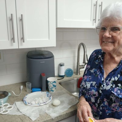 woman smiles with hardboiled egg in hand and air fryer in background