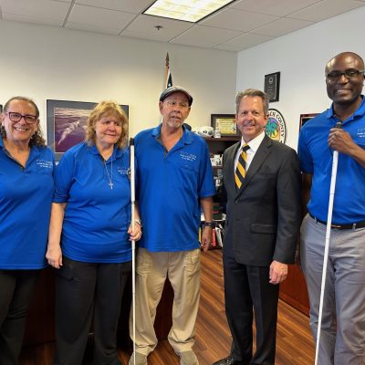 Four adults in blue polo shirts stand with man in black suit and tie.