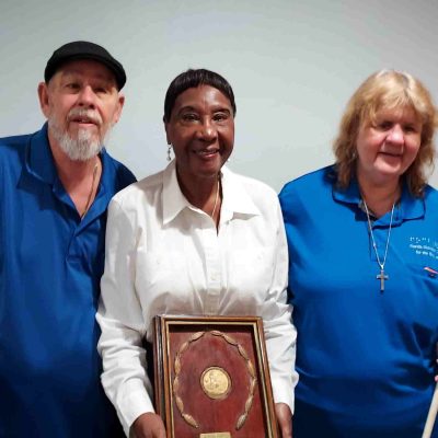 Woman holding certificate stands between man and woman holding a white cane